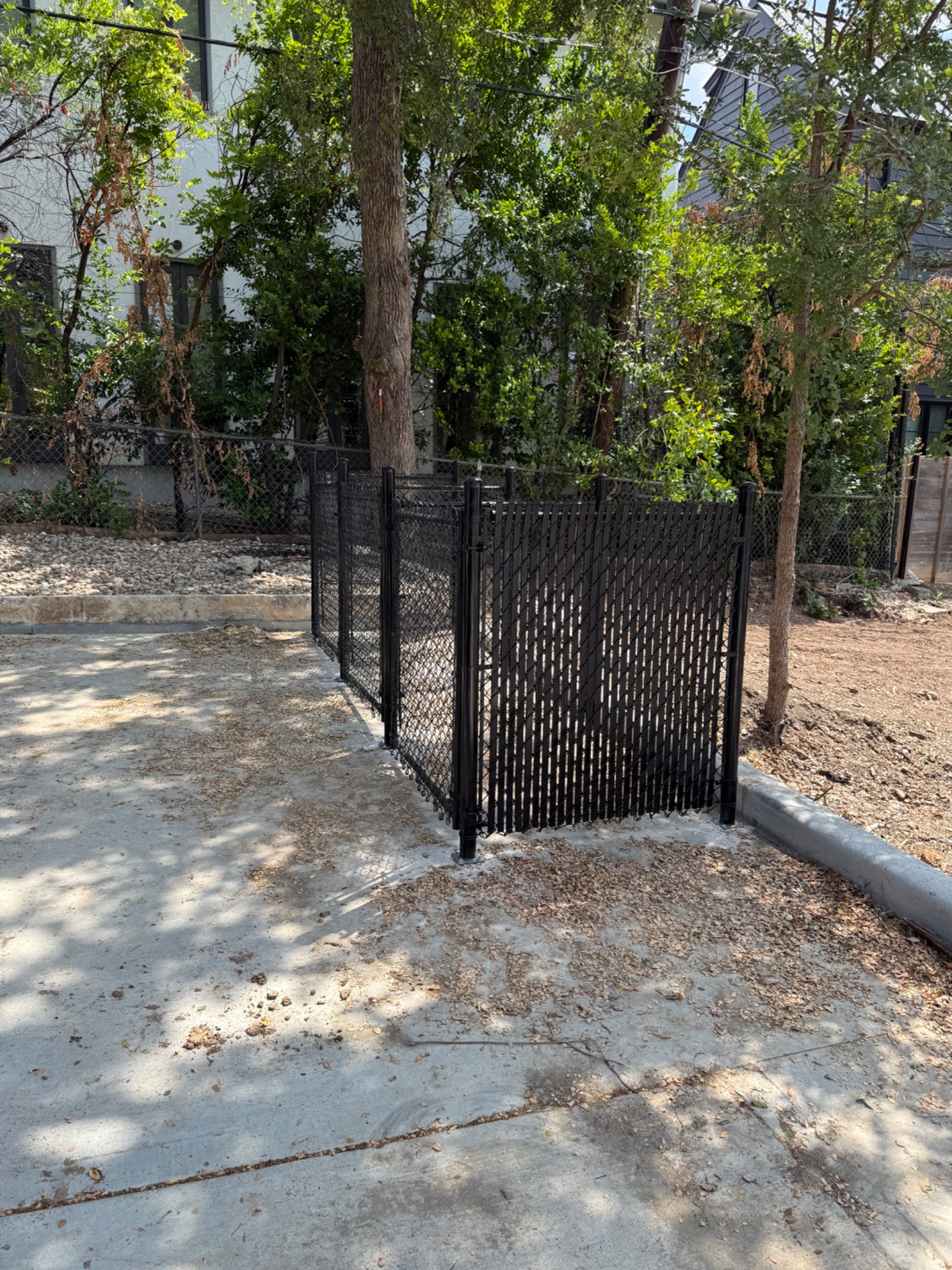 Black vinyl-coated chain link fence with privacy slats for trash enclosure in Austin, TX